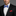Man wearing a black suit with a blue plaid bow tie and red pocket square on a gray background