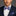 Man wearing a navy suit with a blue plaid bow tie and pocket square on a gray background