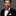 Man wearing a black suit with a white shirt and a red, blue, and white bow tie on a gray background