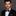 Man wearing a black suit with a green and blue bow tie and pocket square on a gray background