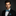 Man wearing a black suit with a blue paisley bow tie and pocket square on a dark background