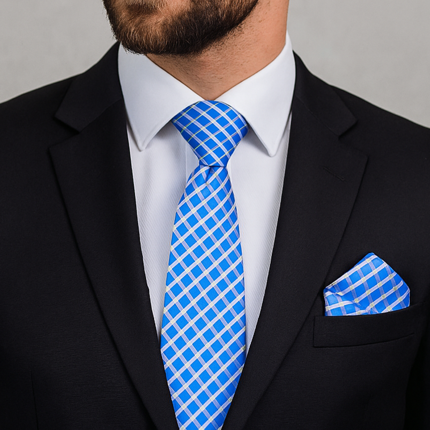 Man wearing a black suit with a blue checkered tie and pocket square against a gray background
