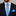Man wearing a black suit with a blue checkered tie and pocket square against a gray background
