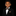 A young boy wearing a black tuxedo jacket, white dress shirt, and a brown and beige patterned bow tie and pocket square, photographed against a solid black background.