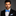 Man wearing a black suit with a white shirt and blue bow tie on a gray background