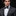 Man wearing a gray suit with a black and white patterned bow tie and pocket square on a black background
