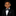 A young boy wearing a black formal suit jacket, white dress shirt, and a black and white paisley bow tie with a matching pocket square, set against a solid black background.