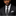 A man wearing a dark charcoal gray suit, white dress shirt, and a patterned dark gray tie with a matching pocket square, set against a solid black background.