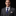 Man wearing a gray suit with a blue tie and patterned pocket square on a black background