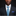 Man wearing a dark suit with a blue and gray patterned tie and pocket square on a black background