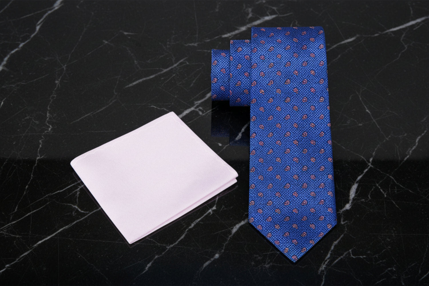 Blue patterned tie and soft pink pocket square on a white background