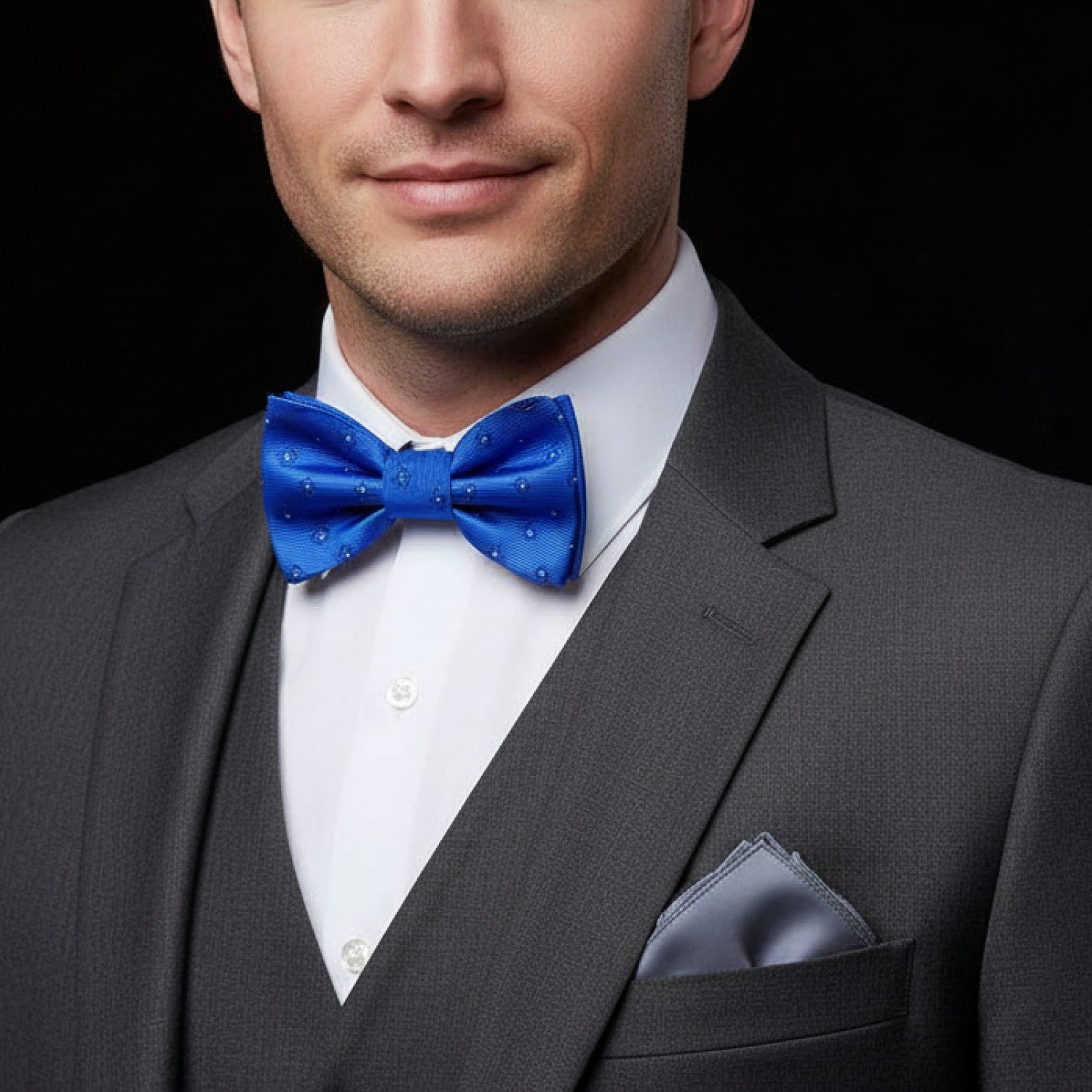 Man wearing a gray suit with a blue bow tie and pocket square on a black background