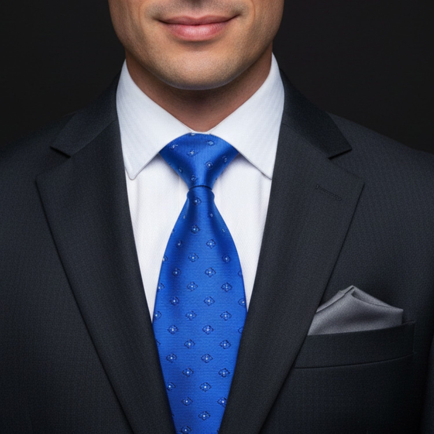 Man wearing a dark suit with a Blue small flowers patterned tie and white shirt against a black background