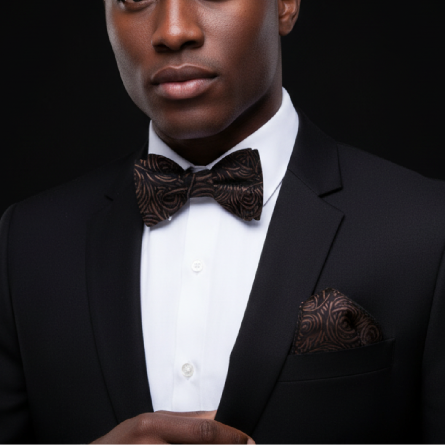 Man wearing a black suit with a patterned bow tie and pocket square on a black background