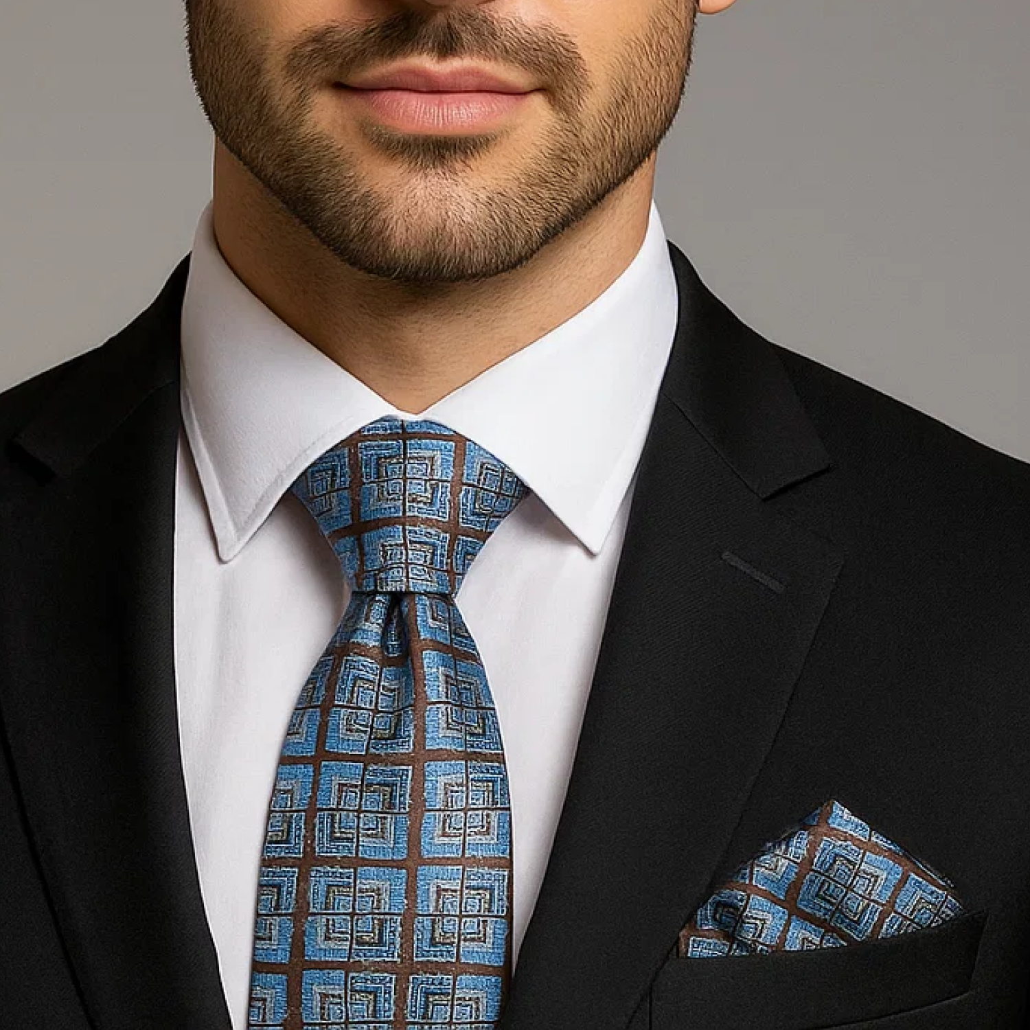 Man wearing a black suit with a blue patterned tie and pocket square against a gray background