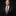 Man wearing a black suit with a red paisley tie and pocket square on a dark background