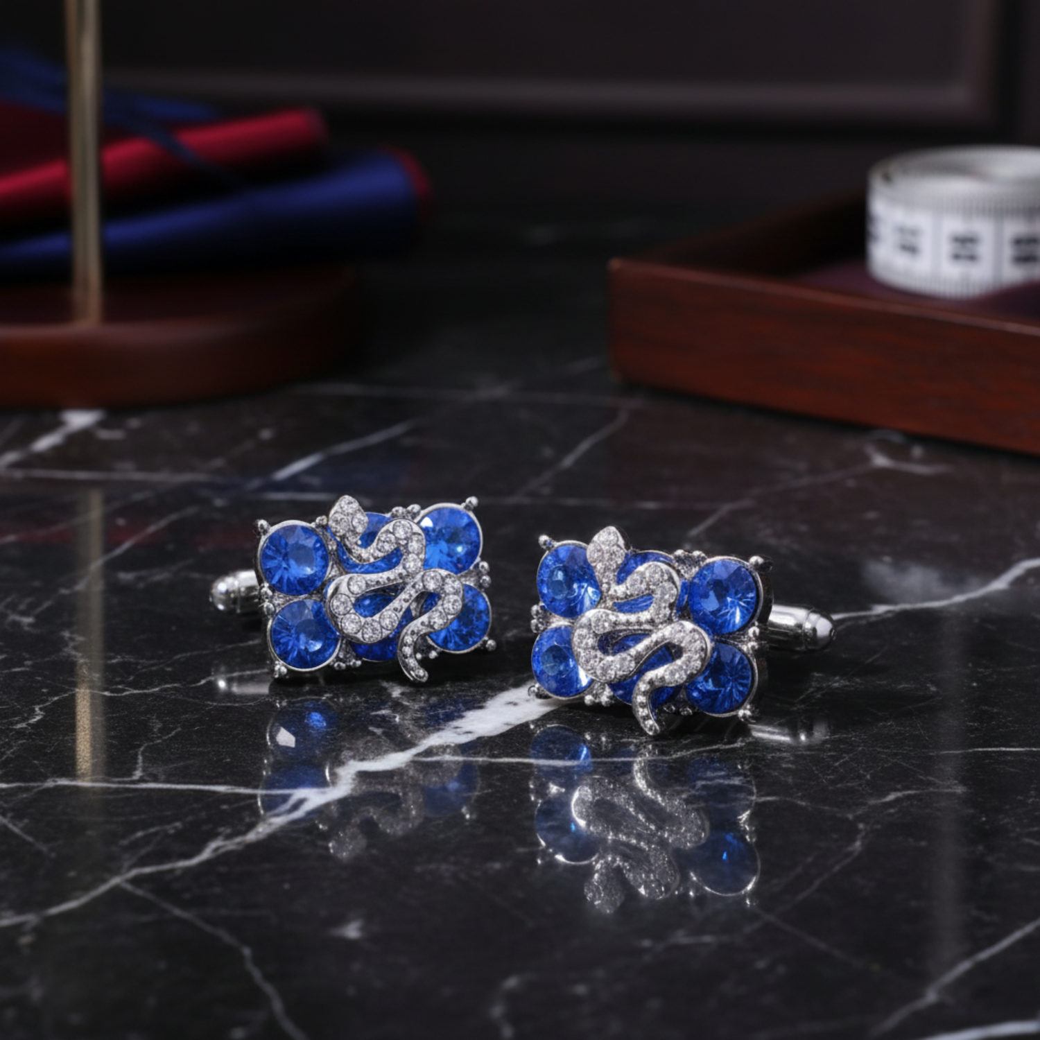 A pair of silver-toned cufflinks featuring blue oval rhinestones and a central scroll motif set with small clear round stones b