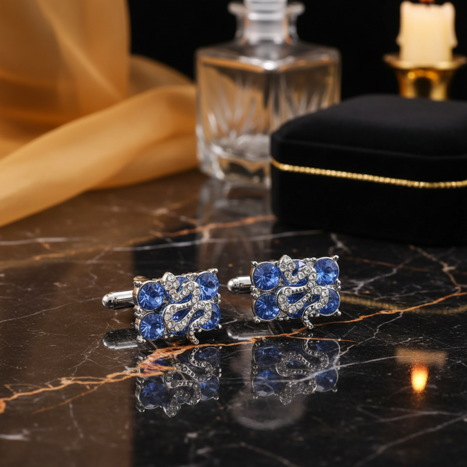 A pair of silver-toned square cufflinks featuring blue crystal flowers with a central silver snake motif, displayed on a textured black surface.