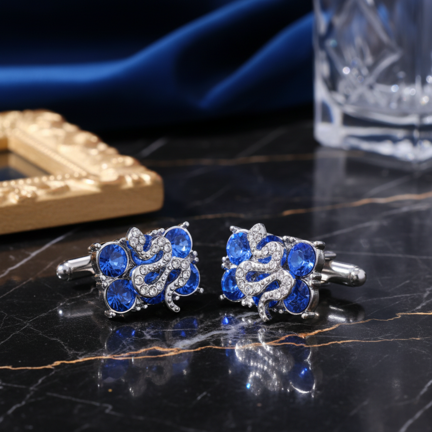 A pair of silver-toned cufflinks with blue crystal accents, one shown from the front and the other from the side/back.  