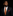 A man in a black suit, white dress shirt, and a patterned orange and brown tie with a matching red pocket square, set against a solid black background.