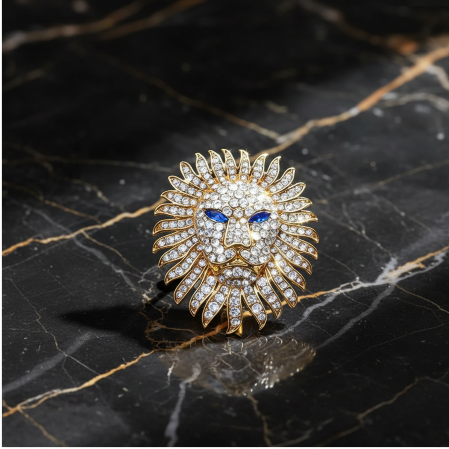 A gold lion head brooch embellished with clear crystals and featuring blue gemstone eyes, displayed on a deep blue velvet fabric background.