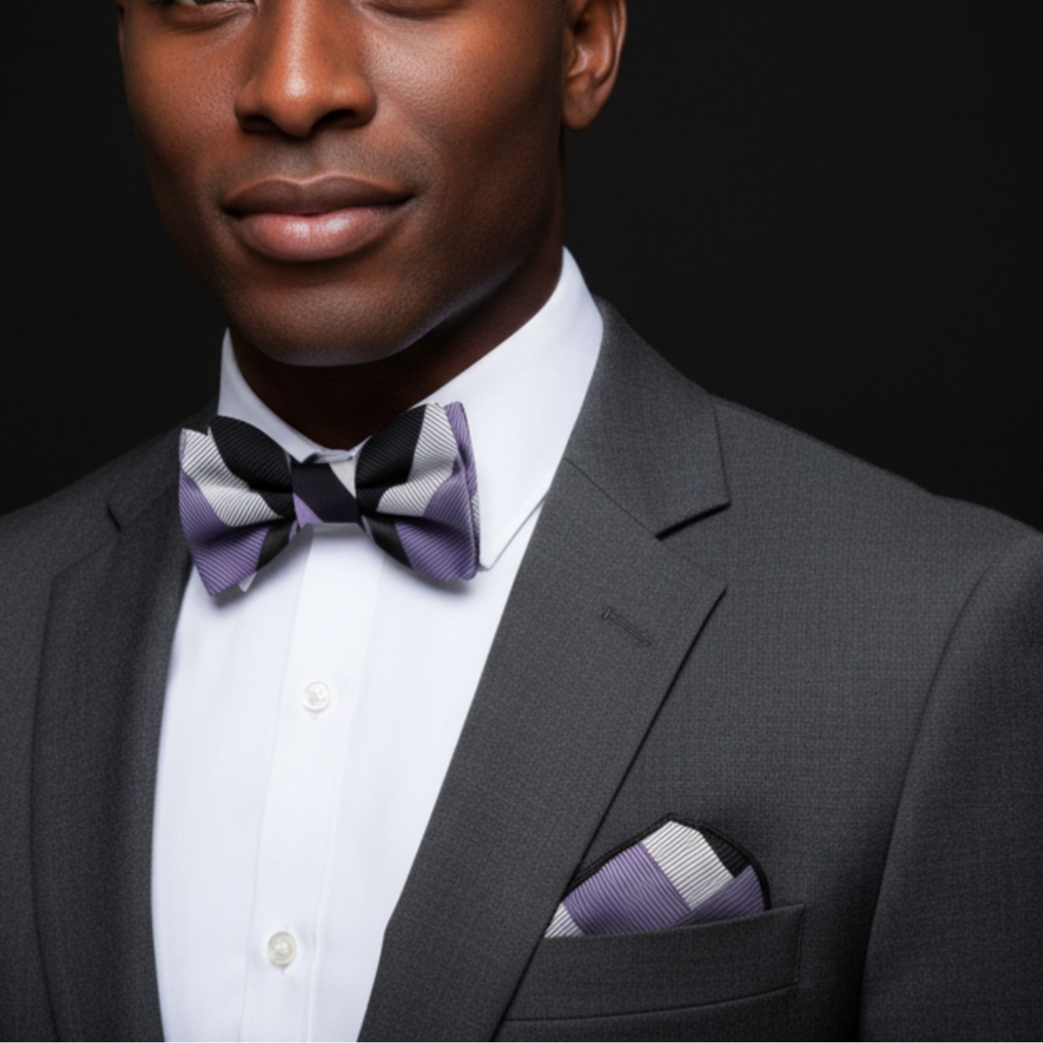 Man wearing a gray suit with a purple bow tie and pocket square against a black background
