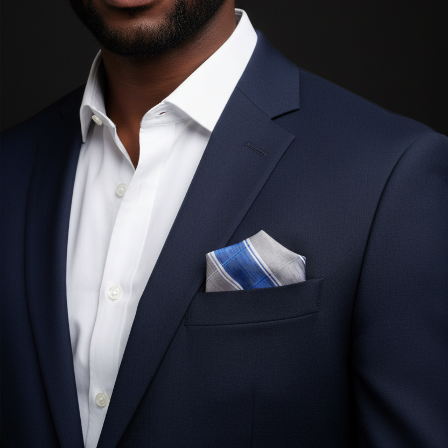 Man wearing a navy suit with a white shirt and patterned pocket square on a black background