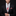 Man wearing a black suit with a plaid tie and red pocket square on a dark background