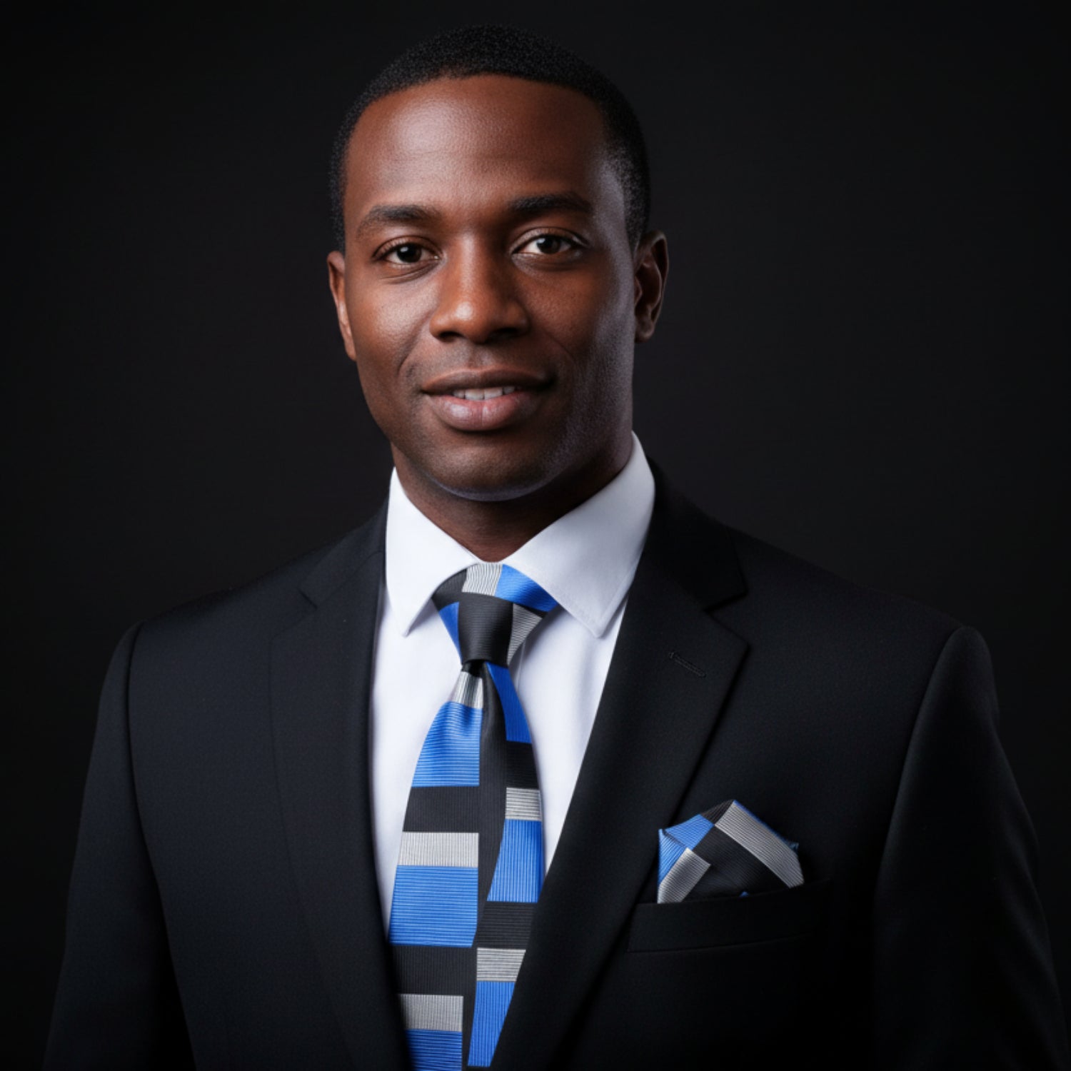Black suit with a blue, black, and gray striped tie and matching pocket square on a white background