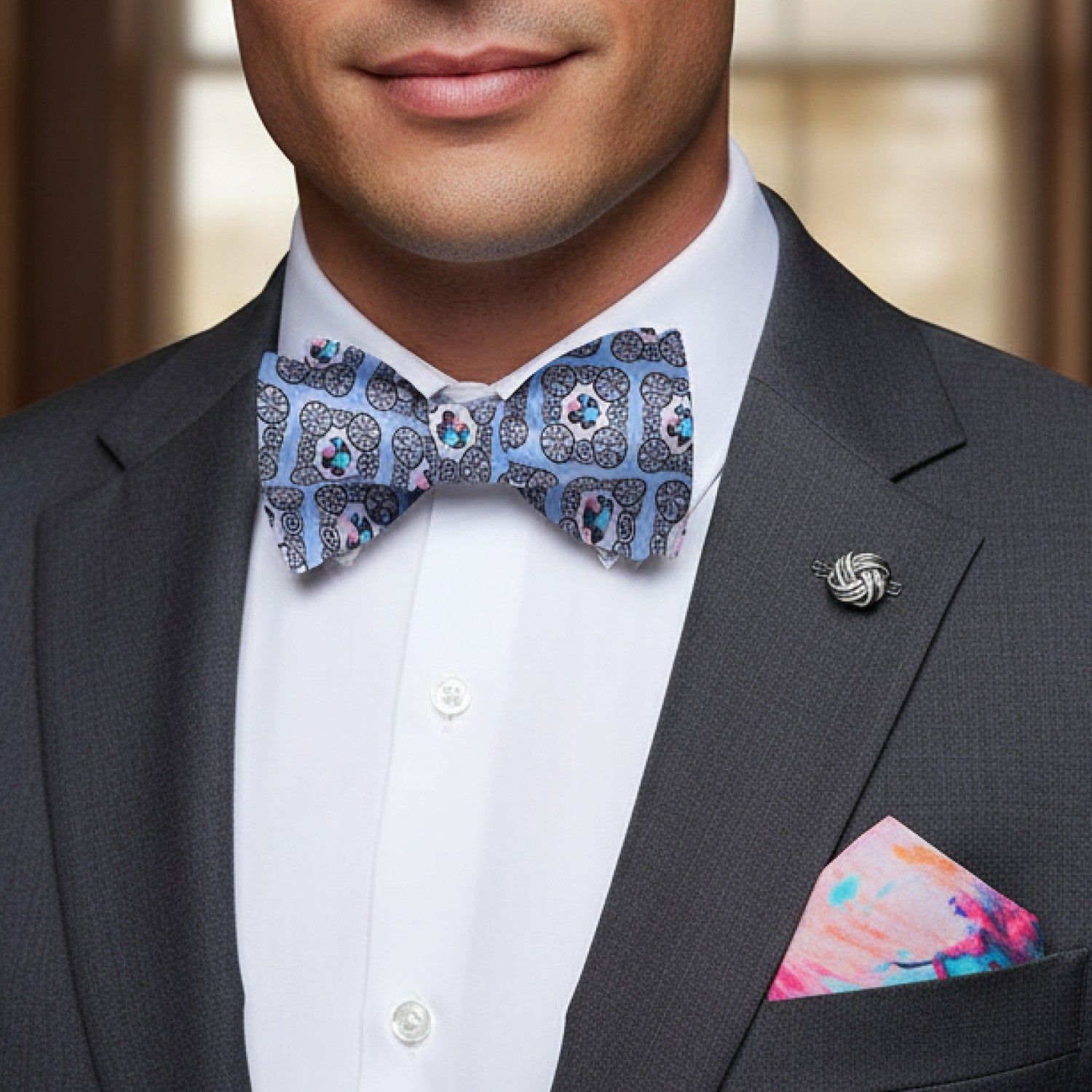 Man wearing a gray suit with a patterned bow tie and colorful pocket square.