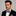 Man wearing a black suit with a plaid bow tie and pink handkerchief on a gray background