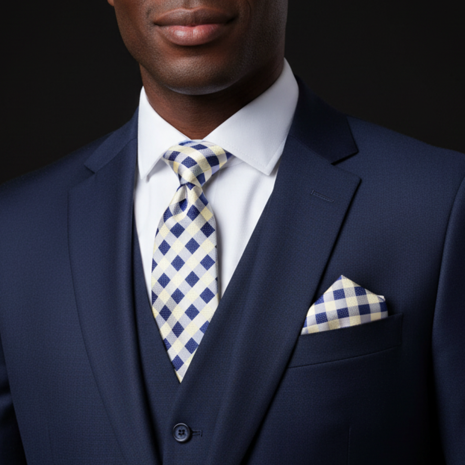 Man wearing a navy suit with a blue and white checkered tie and pocket square on a black background