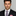 Man wearing a black suit with a plaid tie and pink pocket square on a gray background