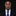 Man wearing a black suit with a blue tie and pocket square on a black background