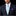 A man wearing a dark navy suit, white dress shirt, a light blue and white patterned tie, and a purple pocket square, photographed against a solid black background.