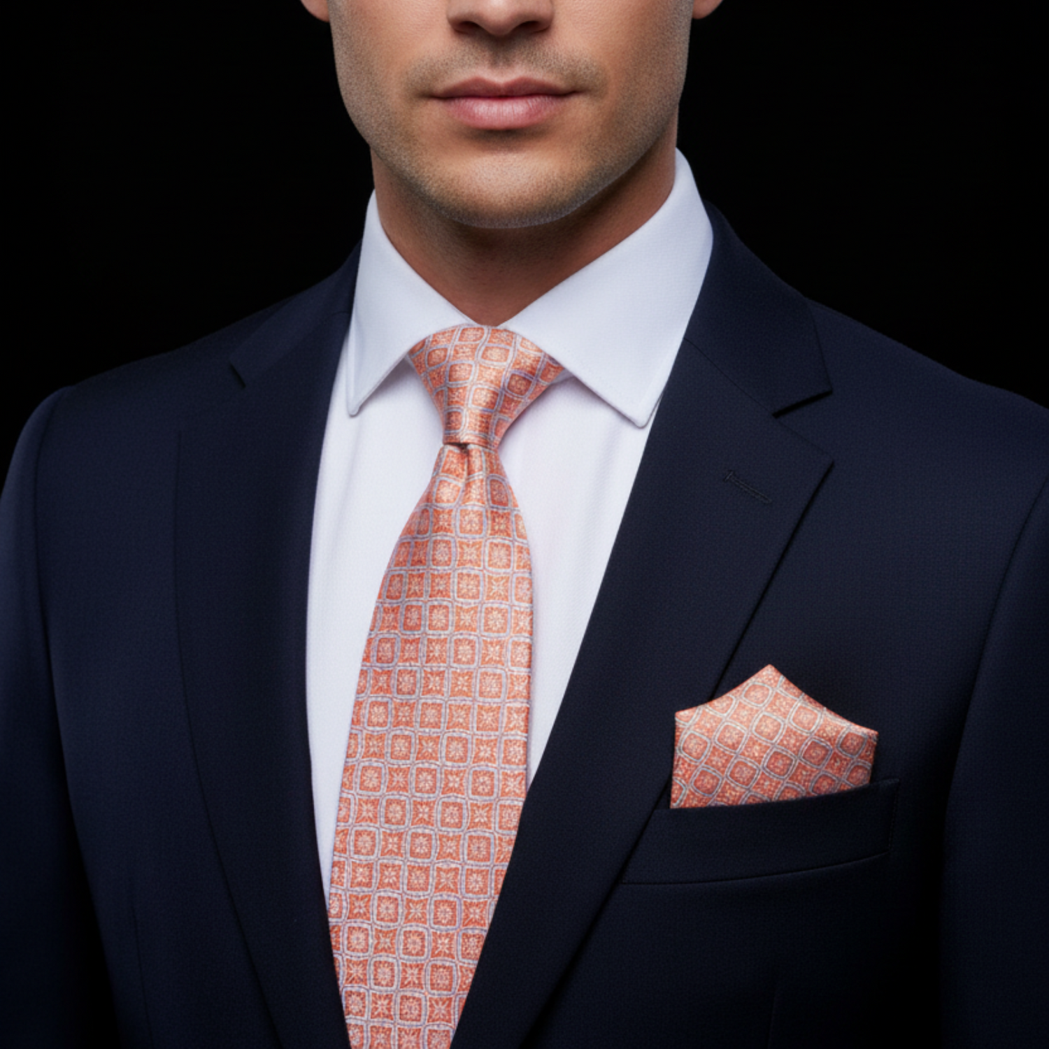 Man wearing a navy suit with an orange patterned tie and pocket square on a black background