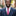 Man in a navy suit with a pink tie standing on a city street