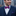 Man wearing a navy suit with a colorful bow tie and pocket square, standing against an urban background.