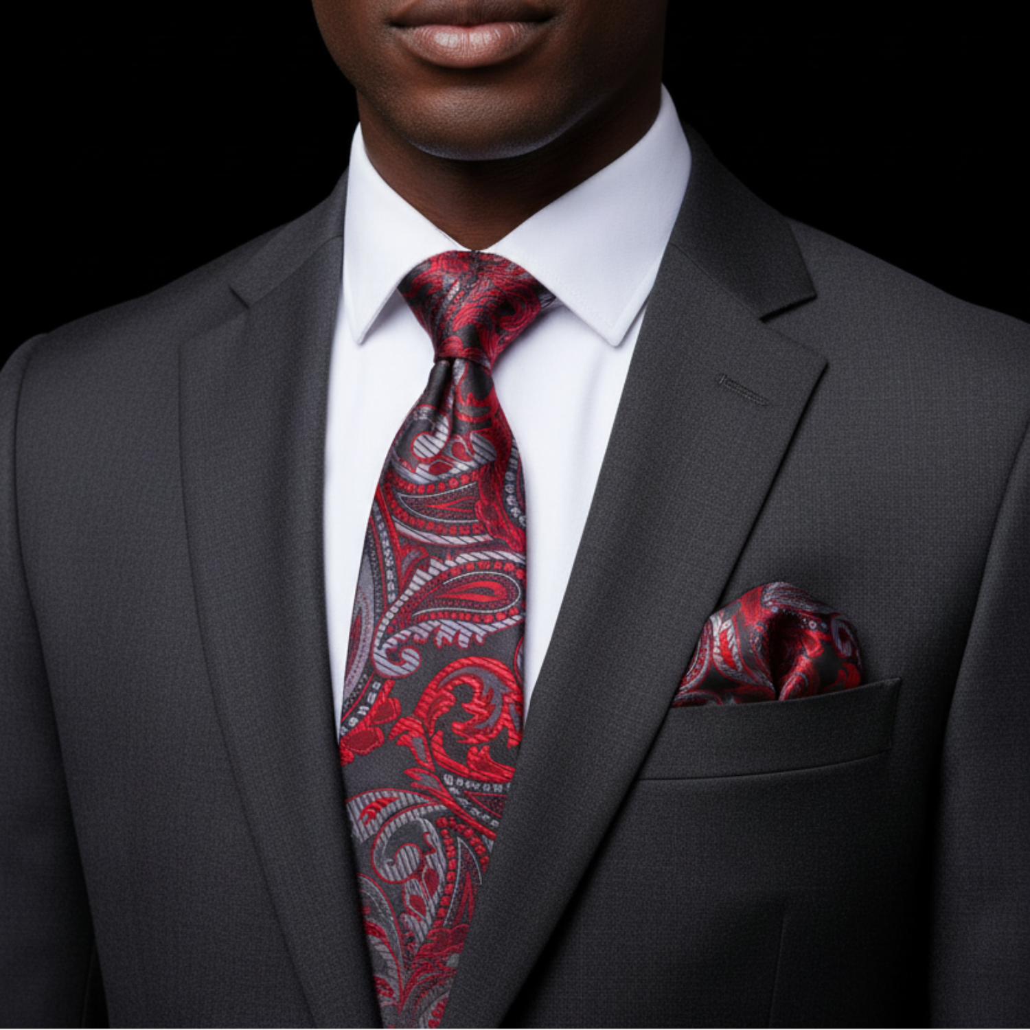 Man wearing a gray suit with a red paisley tie and pocket square against a black background