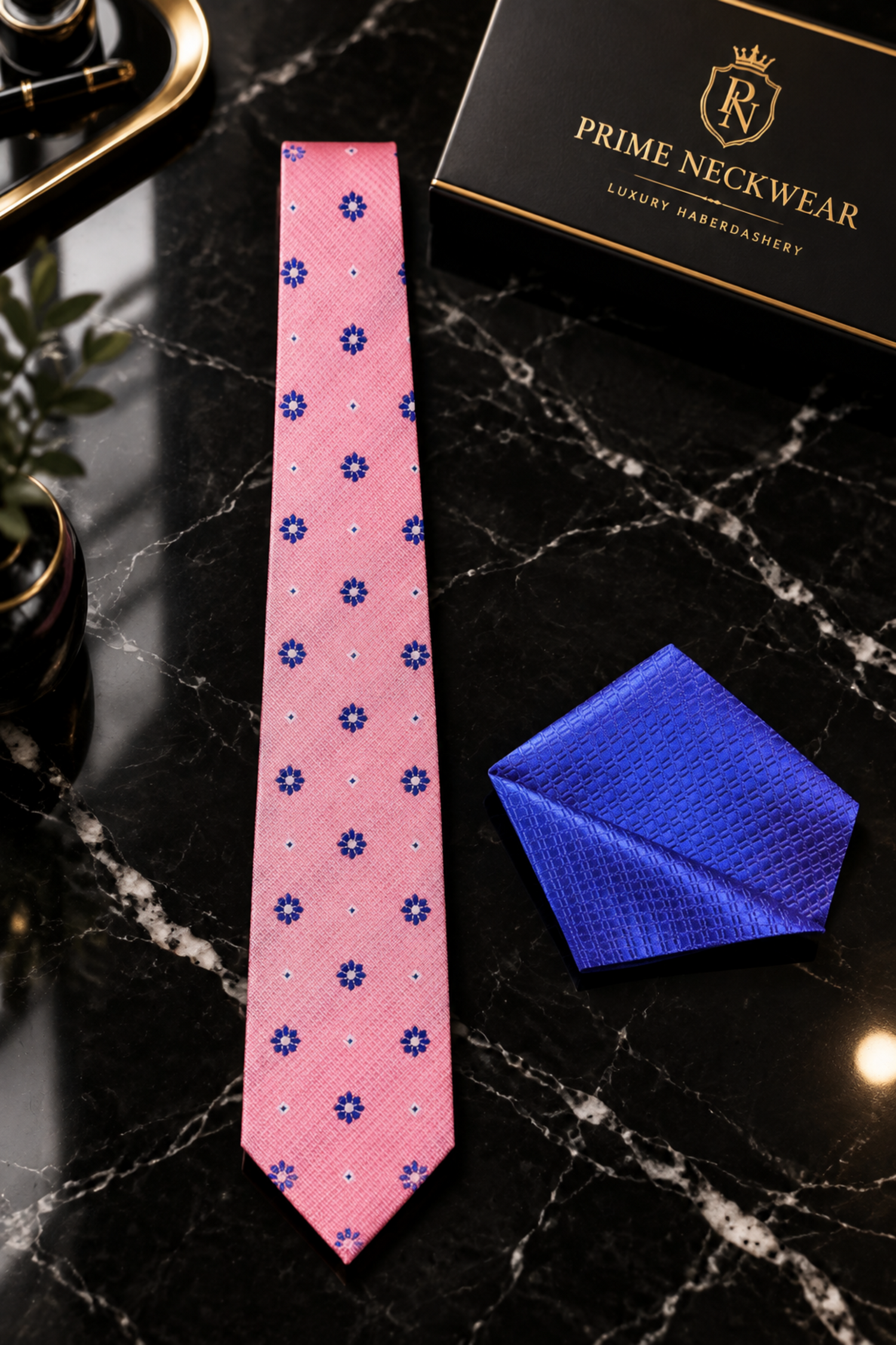 A pink necktie with a navy blue and white floral pattern, styled with a matching textured blue pocket square on a black suit jacket and white dress shirt.
