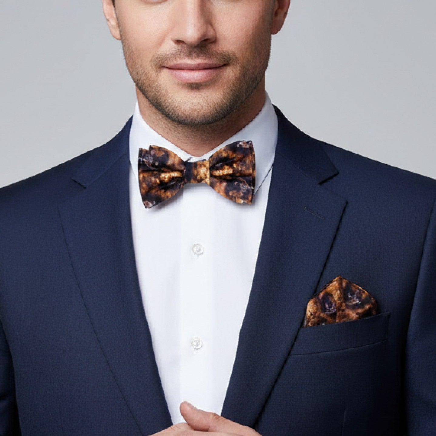 Man wearing a navy suit with a leopard print bow tie and pocket square on a gray background