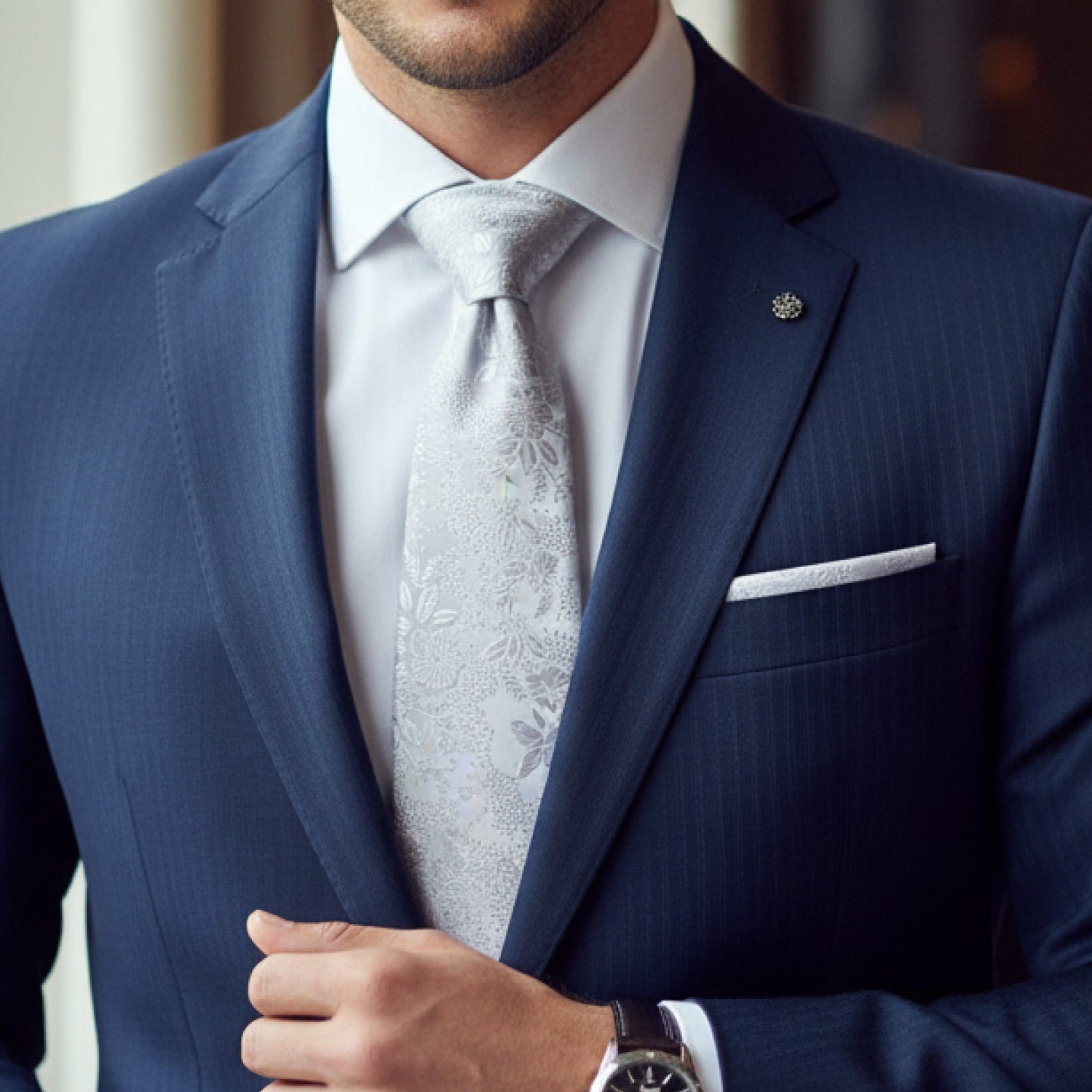 Man wearing a blue suit with a white shirt and patterned tie.