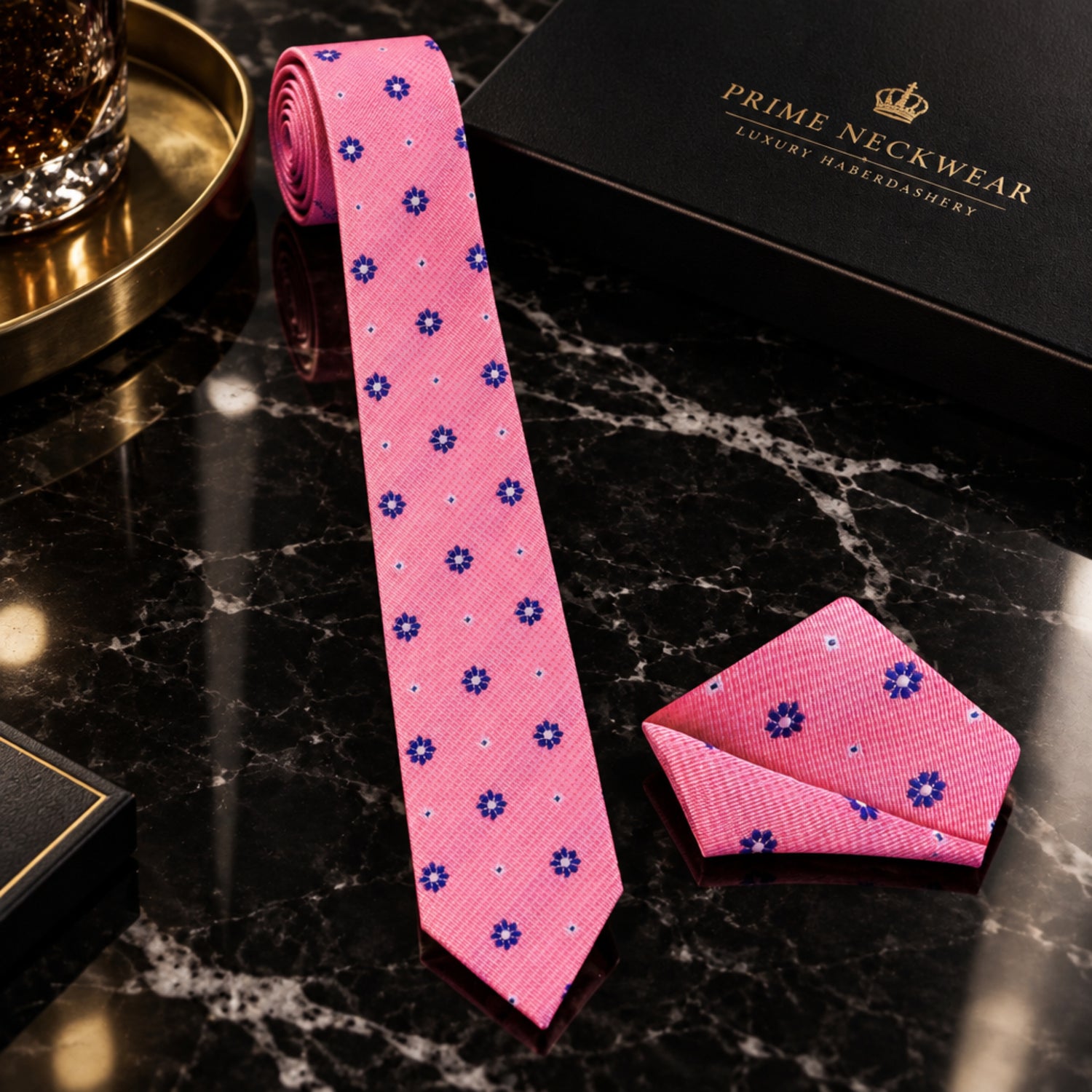 A pink necktie and matching pocket square set with a small blue and white floral pattern, styled on a white dress shirt and black suit jacket.