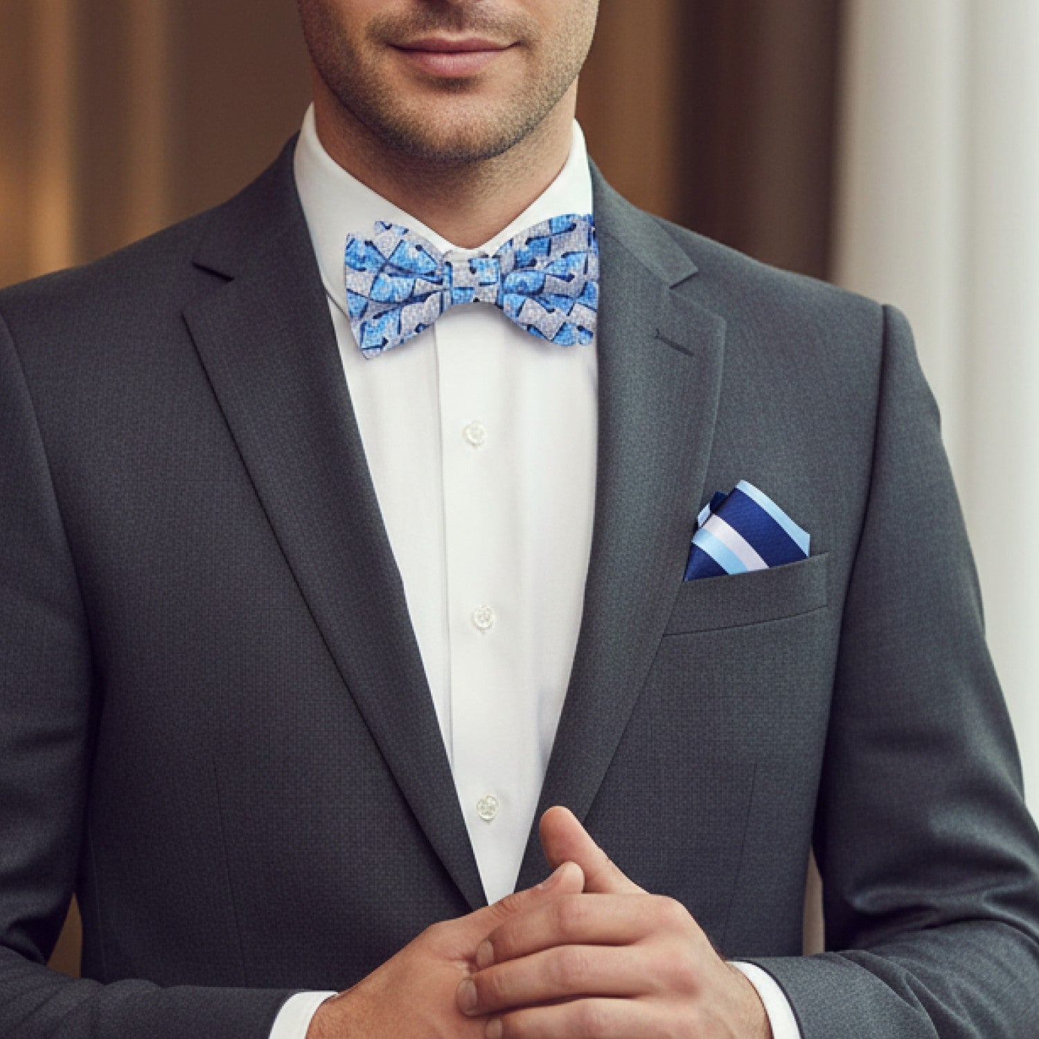 Man wearing a gray suit with a blue patterned bow tie and matching pocket square.