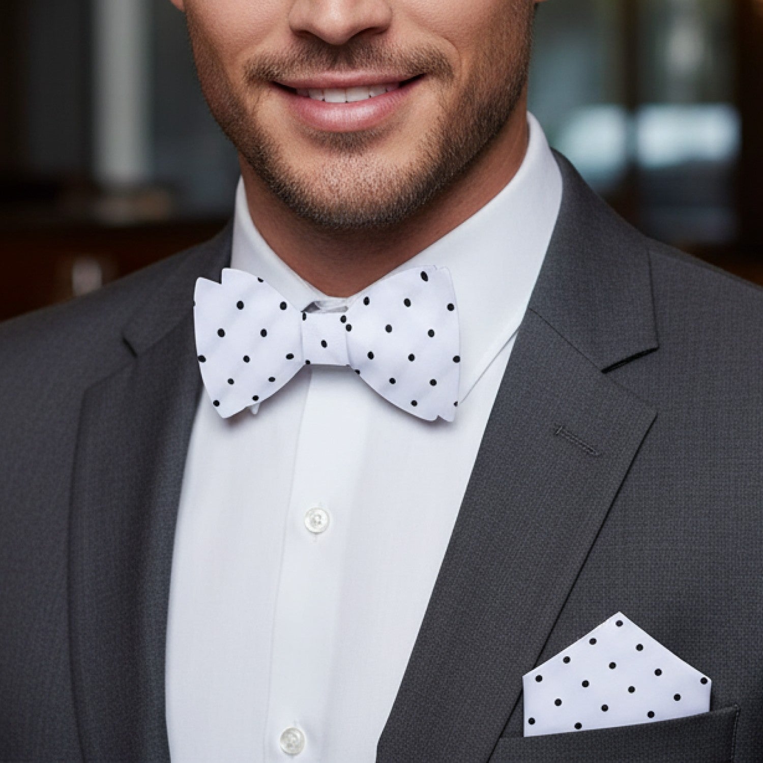 Man wearing a gray suit with a white shirt, polka dot bow tie, and pocket square.