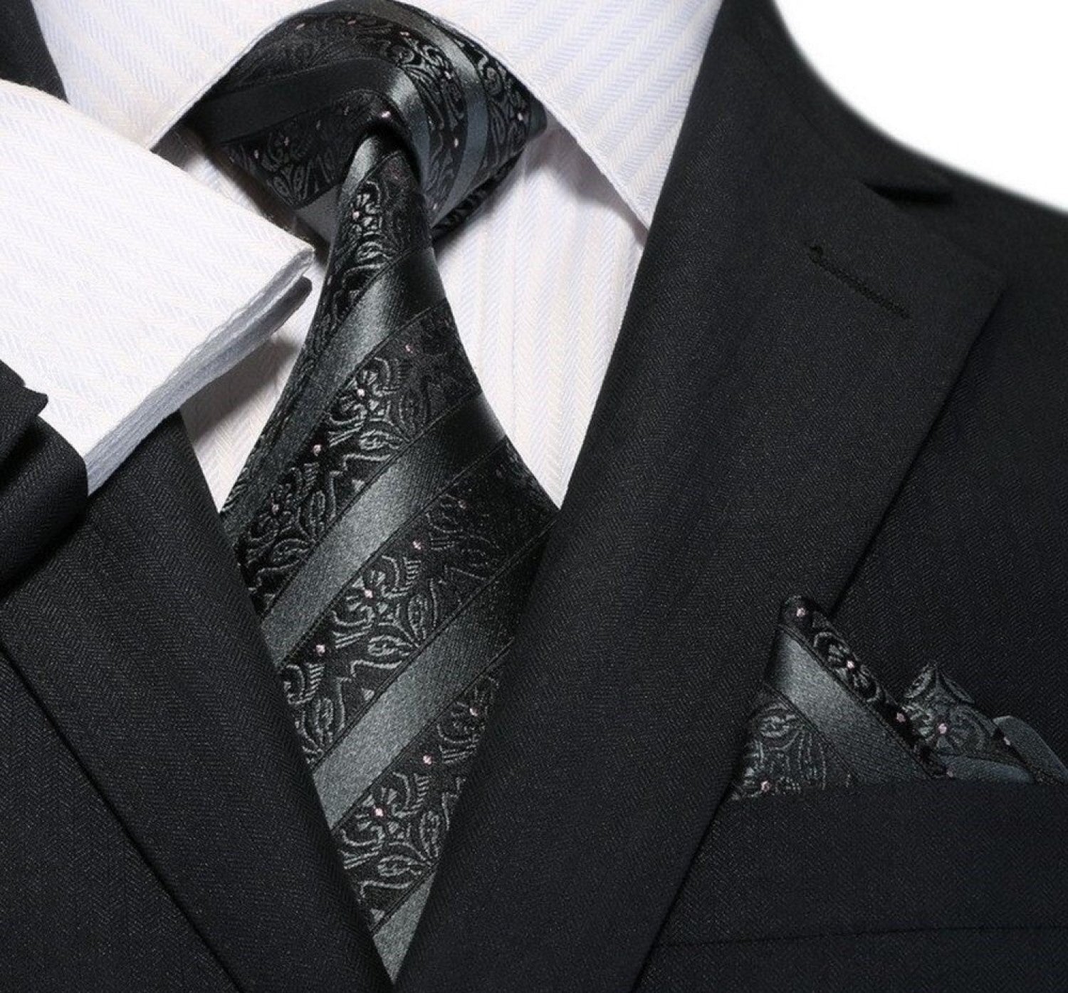 Black suit with a patterned black tie and pocket square on a white background