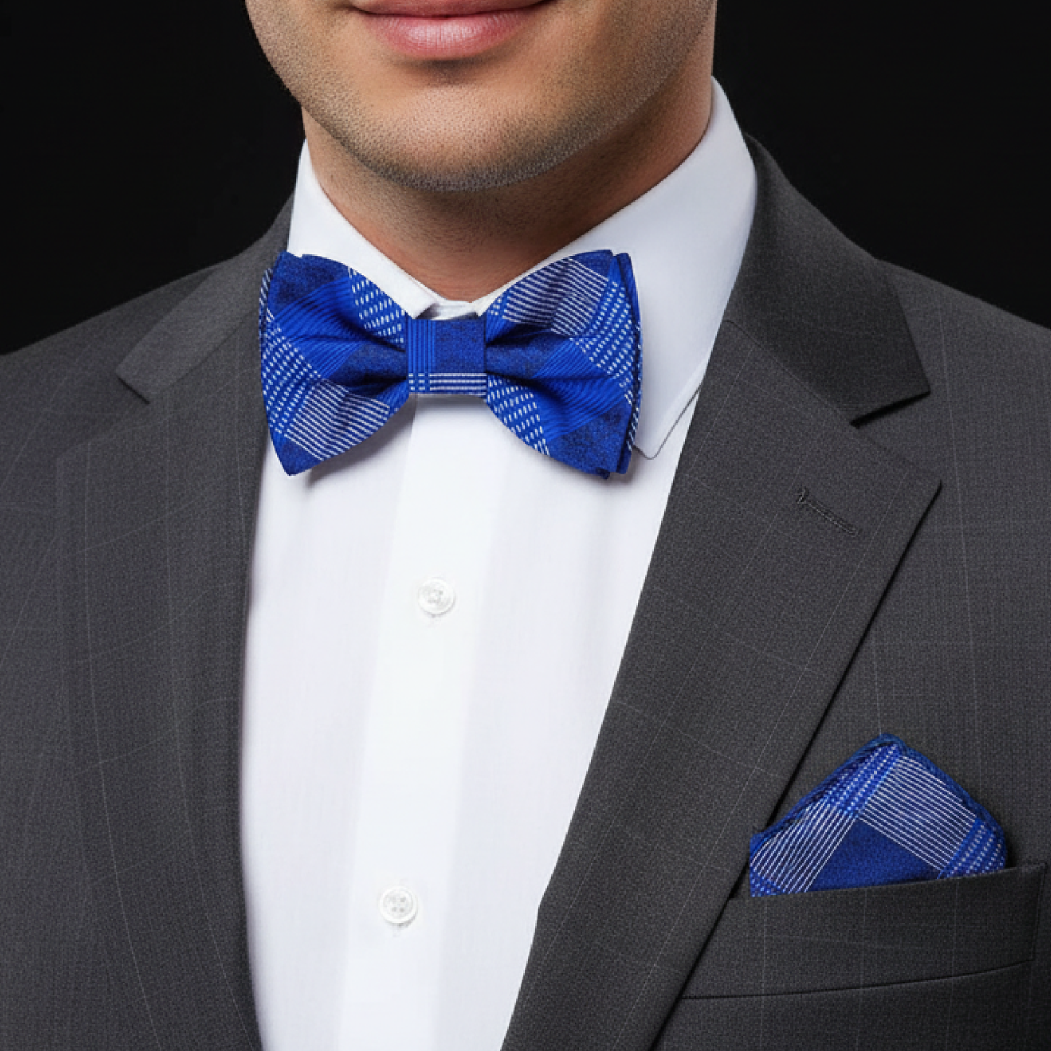 Man wearing a gray suit with a blue plaid bow tie and pocket square on a black background