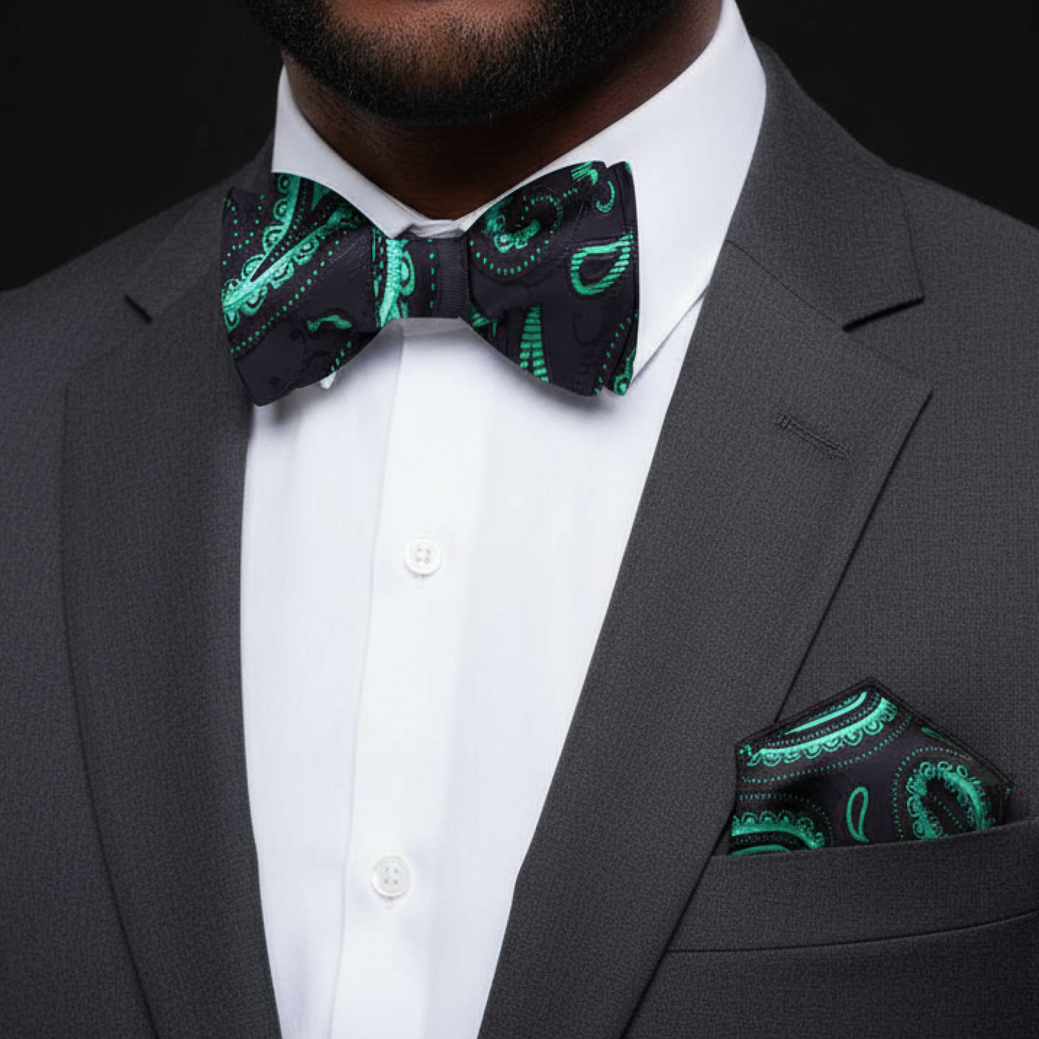 Man wearing a gray suit with a green and black patterned bow tie and pocket square.