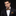 Man wearing a black suit with a patterned bow tie and pocket square on a dark background
