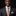 Man wearing a dark suit with an orange and brown striped tie and pocket square on a black background